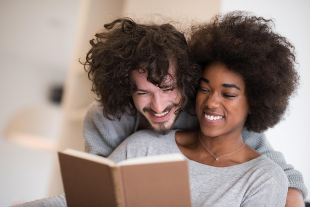 Joven pareja multiétnica hermosa abrazándose frente a la chimenea en casa cuando lee un libro en el día de otoño