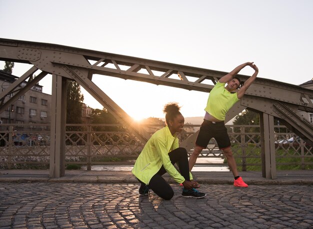 Joven pareja multiétnica de jogging calentándose y estirándose antes de correr por la mañana en la ciudad