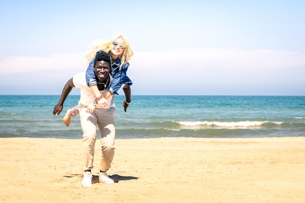 Joven pareja multirracial en la playa divirtiéndose con piggyback jump