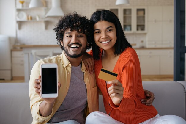 Joven pareja multirracial sonriente con tarjeta de crédito usando una aplicación móvil para compras en línea