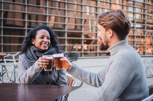 Una joven pareja de negocios bebiendo cerveza hablando y elevando un brindis en la terraza de un pub de la ciudad concepto de estilo de vida