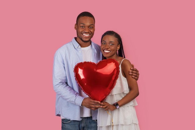 Joven pareja negra romántica abrazándose y sosteniendo un globo en forma de corazón