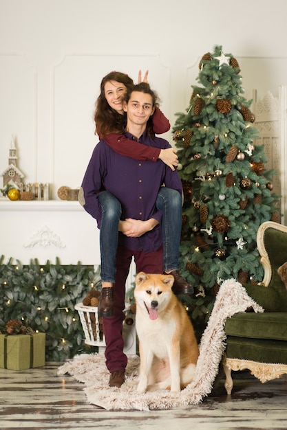 Una joven pareja con un perro jugando cerca de un árbol de navidad. feliz año nuevo y feliz navidad