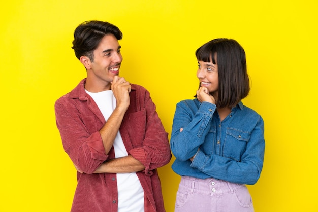 Una joven pareja de raza mixta aislada de fondo amarillo mirando el uno al otro