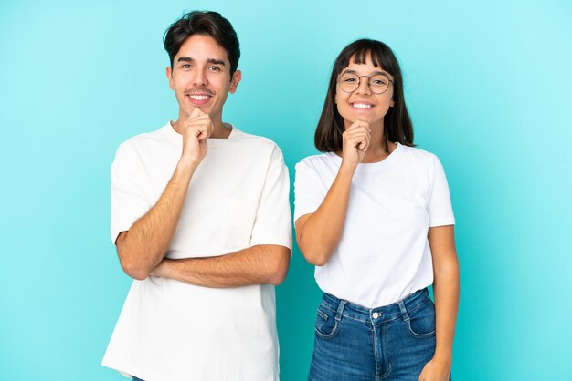 Joven pareja de raza mixta aislada de fondo azul sonriendo y mirando al frente con cara de confianza