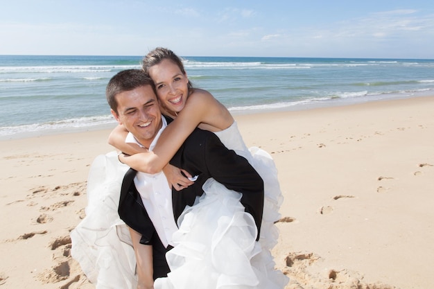 Una joven pareja recién casada en una playa a cuestas