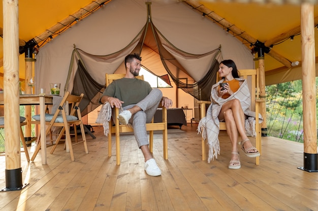 Joven pareja relajada sentados en sillones en el patio de la carpa glamping