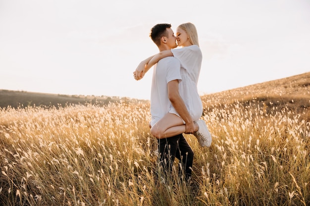 Joven pareja romántica en un campo divirtiéndose, abrazándose y besándose.
