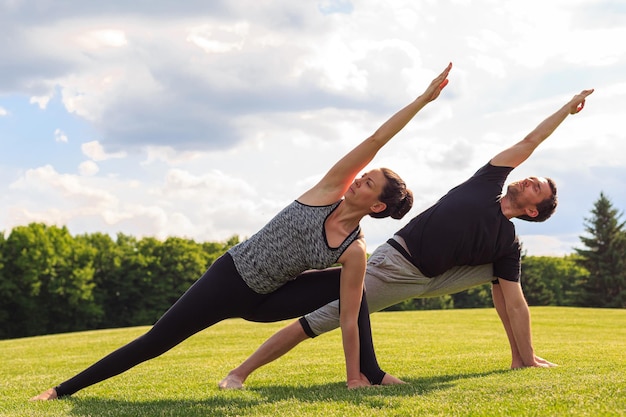 Joven pareja sana haciendo yoga en el soleado parque de verano Fitness y estilo de vida saludable