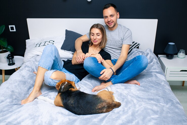 Joven pareja sentada en una cama en el dormitorio, abrazándose. Cerca de ellos está su perro