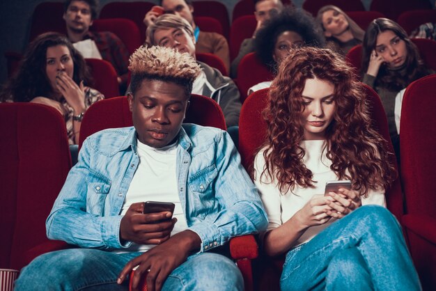 Foto joven pareja está sentada en el cine mirando los teléfonos.