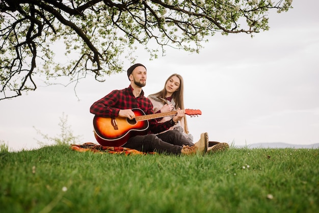 Joven pareja sentada bajo el gran árbol y el hombre tocando la guitarra