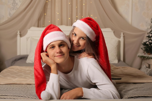 Una joven pareja con sombreros de Santa Claus está acostada en la cama sonriendo Navidad