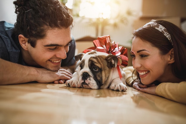 Una joven pareja sonriente disfrutando con su cachorro de bulldog inglés mientras se muda a su nuevo hogar.