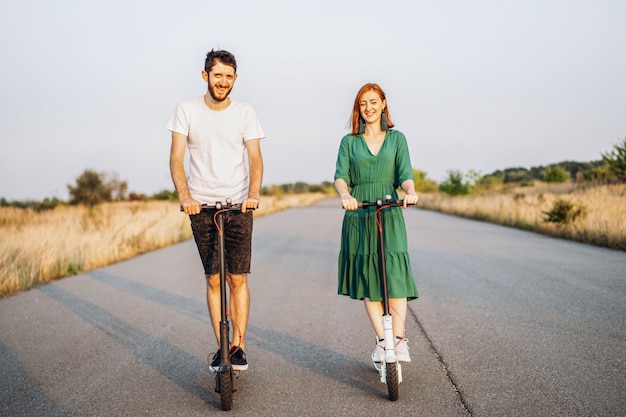 Joven pareja sonriente feliz divirtiéndose conduciendo scooter eléctrico en la carretera en el campo. Tecnologías de contenido