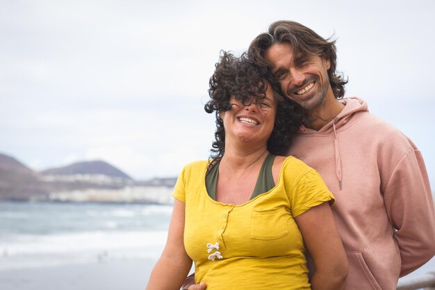 Joven pareja sonriente junto al mar en un día ventoso en Las Palmas Islas Canarias Felices padres esperando