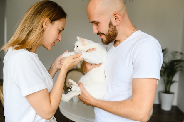 Una joven pareja sostiene un gato blanco en sus brazos