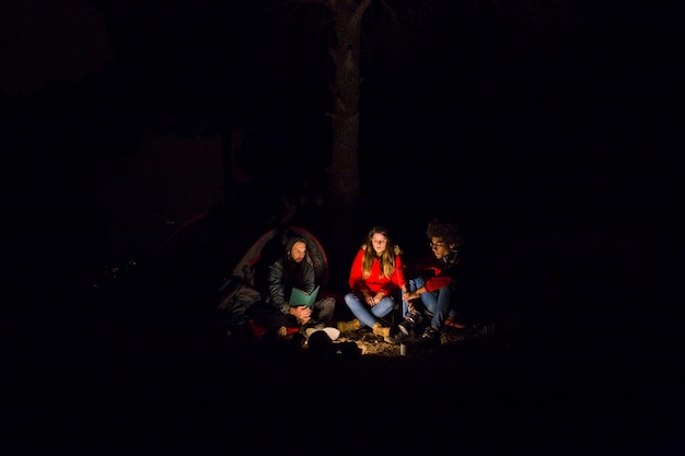 Joven pareja y su amigo disfrutando en el campamento por la noche