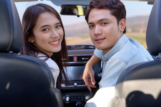 Joven pareja en su coche, feliz de conducir en un camino rural. Felices mujeres jóvenes y hombres jóvenes en coche