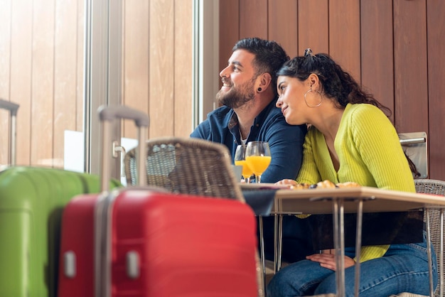 Joven pareja de turistas desayunando en un hotel y mirando por la ventana