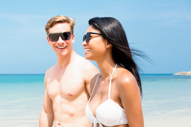 Joven pareja de turistas interraciales paseando por la playa