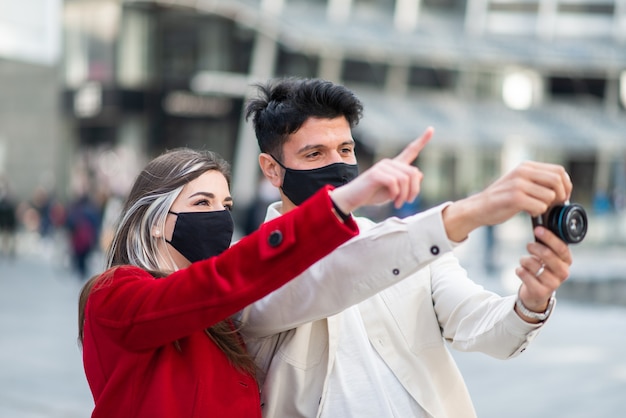 Joven pareja de turistas tomando fotografías en una ciudad durante la pandemia de covid o coronavirus