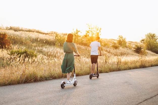 Joven pareja de vacaciones divirtiéndose conduciendo scooter eléctrico en la carretera en el campo. Tecnologías de contenido. Vista trasera