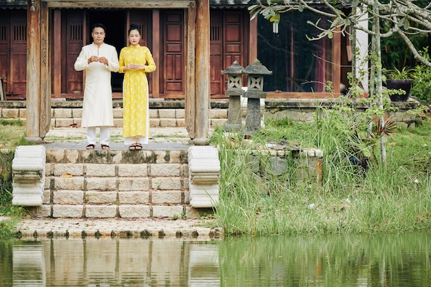 Joven pareja vietnamita en ao dai vestido de pie con varitas de incienso delante del templo