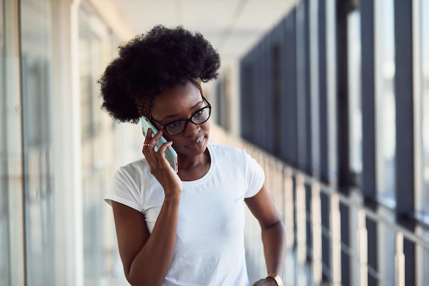 Una joven pasajera afroamericana con ropa informal está en el aeropuerto con teléfono.