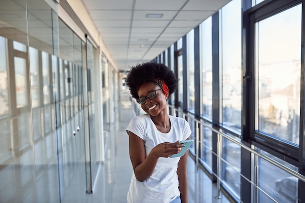 Una joven pasajera afroamericana con ropa informal está en el aeropuerto con teléfono.