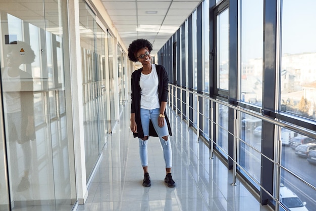 Una joven pasajera afroamericana con ropa informal está en el aeropuerto.