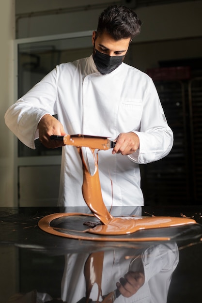 Joven pastelero con máscara trabajando en templar el chocolate.