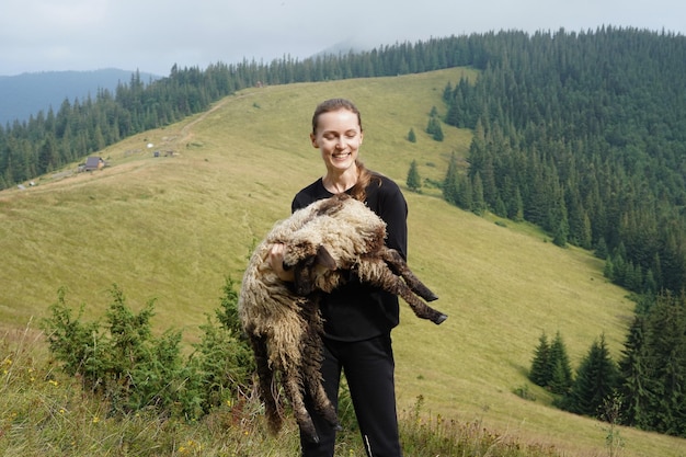 Joven pastora bonita riendo y sosteniendo una oveja El concepto de amor por la naturaleza, el cuidado de los animales y el ecoturismo