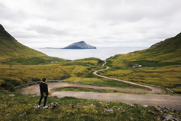 Joven patinador con su patineta mira un camino sinuoso en las islas feroe