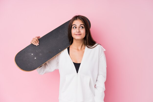 Joven patinadora caucásica mujer sosteniendo skate soñando con lograr objetivos y propósitos