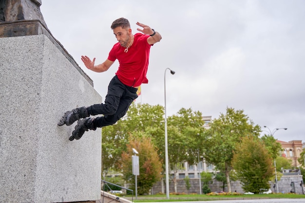 joven patinando en patines en línea saltando sobre la pared de la ciudad