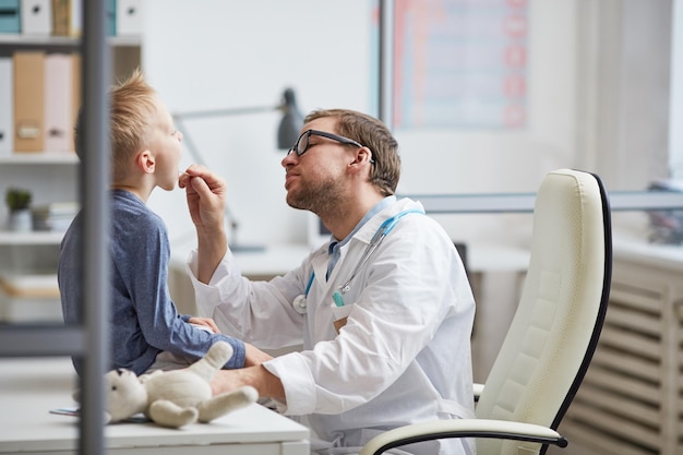 Joven pediatra revisando la garganta de los niños