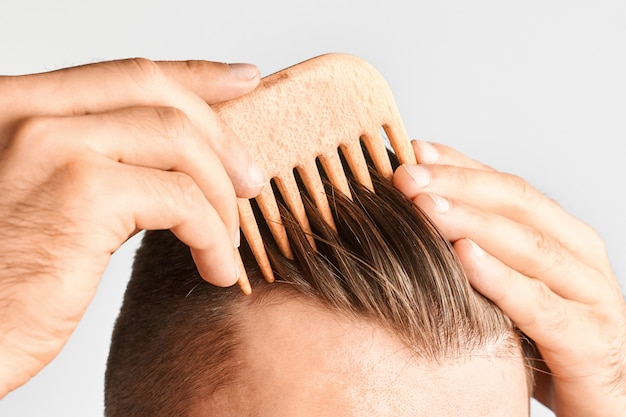 Joven peinado con un peine de madera. Peinado en casa. Concepto publicitario de champú para un cabello sano y contra la caspa.