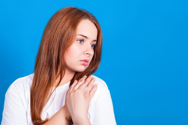 Joven pelirroja atractiva tristemente mira hacia otro lado Foto de estudio sobre un fondo azul