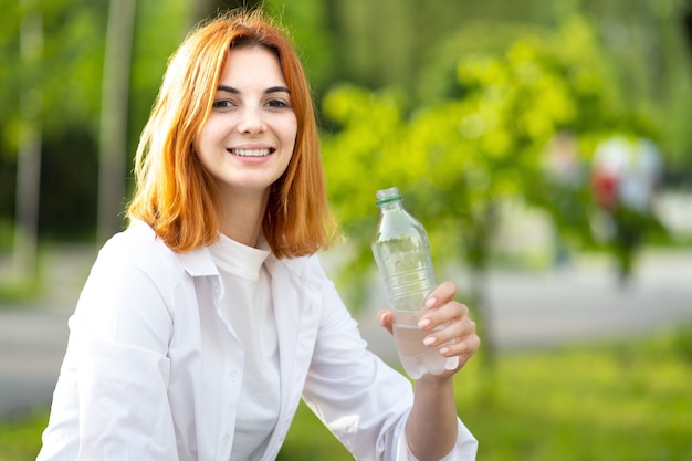 Joven pelirroja bebiendo agua de una botella el día de verano.