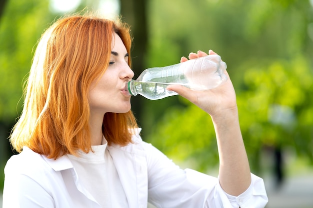 Joven pelirroja bebiendo agua de una botella en verano