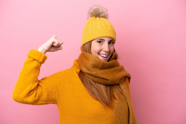 Joven pelirroja con chaqueta de invierno aislada de fondo rosa haciendo un gesto fuerte