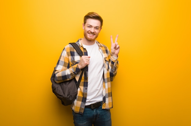 Joven pelirroja estudiante hombre divertido y feliz haciendo un gesto de victoria