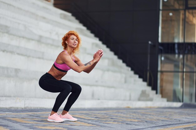 Joven pelirroja europea con ropa deportiva haciendo sentadillas al aire libre