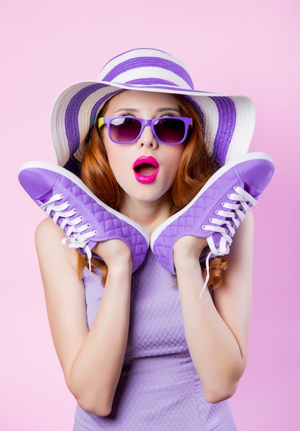 Joven pelirroja con gafas de sol y sombrero con zapatos en rosa