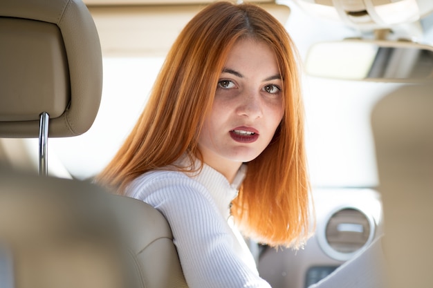 Joven pelirroja mujer conductora conduciendo un coche hacia atrás.