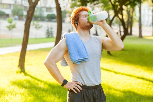 Joven pelirroja y pecas hombre bebe agua después de cruzar y cerrar los ojos