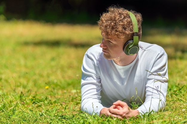 Joven pelirrojo en auriculares se encuentra sobre la hierba verde en un día soleado