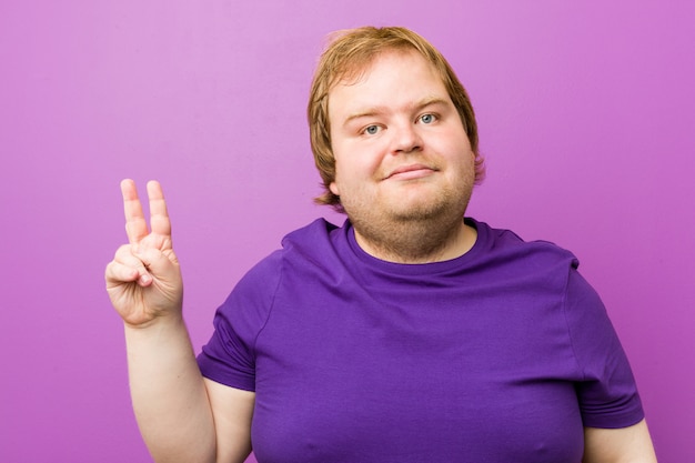 Joven pelirrojo auténtico gordo alegre y despreocupado mostrando un símbolo de paz con los dedos.