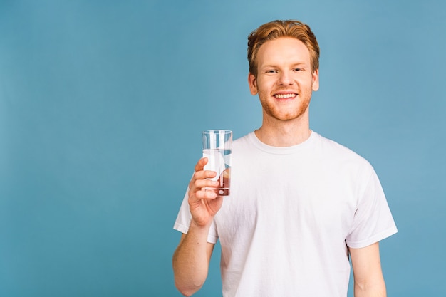 un joven pelirrojo con una camiseta blanca bebiendo agua de un vaso.